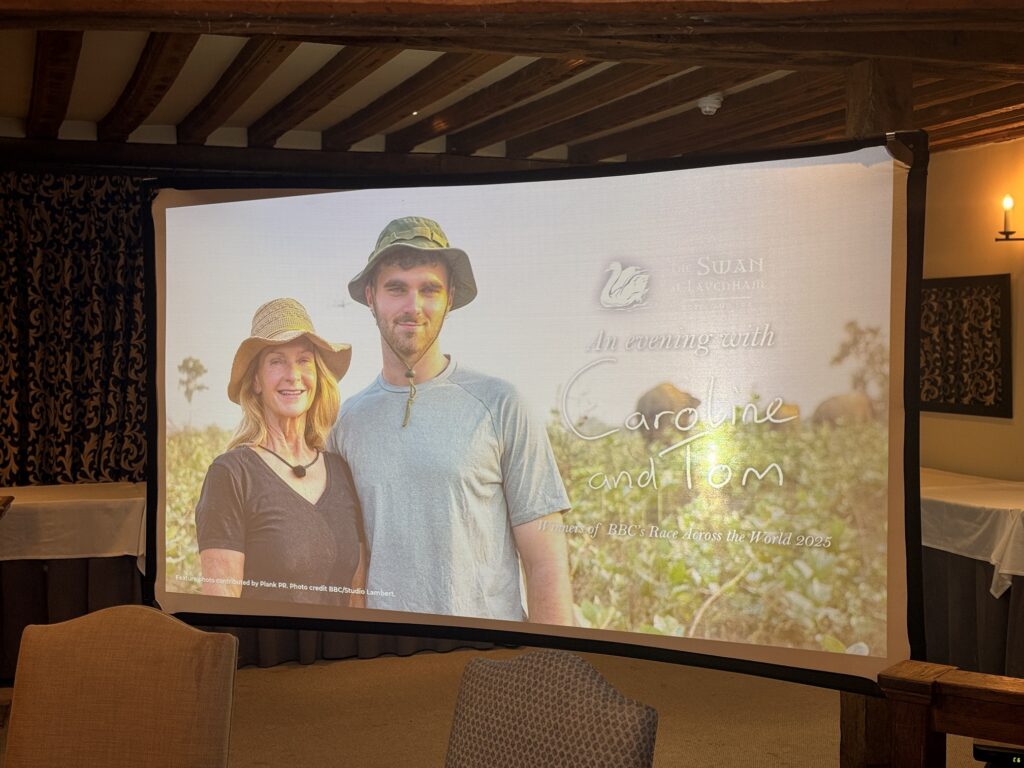 A projector screen showing an image of Caroline and Tom from BBC's Race Across the World