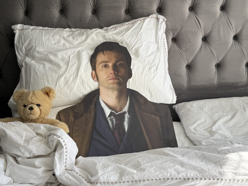 A life-size cardboard cutout of David Tennant in bed next to a teddy bear
